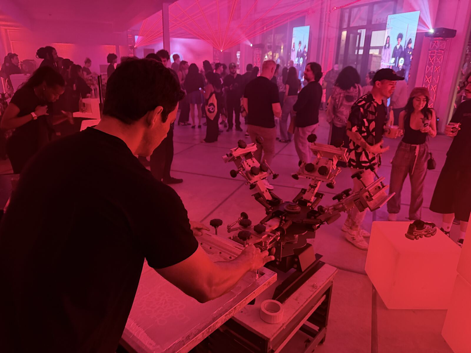 Crowded event booth with attendees gathered around live printing stations under magenta stage lighting